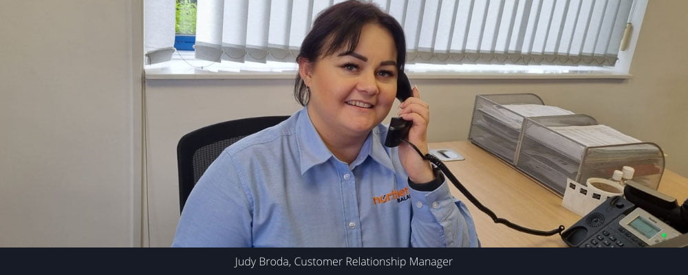 Judy sits behind a desk smiling at the camera while holding a phone to her ear, Enhancing our partnership approach to enable customer success
